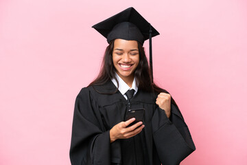 Young university Colombian woman graduate isolated on pink background with phone in victory position