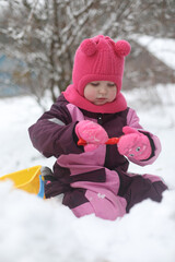 Adorable girl dig snow with shovel and pail on playground covered with snow. little girl playing in winter outdoors