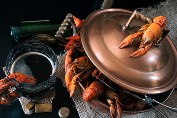 Luxury seafood dinner - prepared crayfish in a vintage copper pot and a glass of craft dark beer