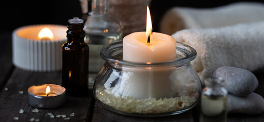 Spa setting with essential oil, candle, sea salt, pebbles, towel on dark wooden background. Massage, aromatherapy. Natural organic ingredients for relaxation, detention, wellness. Banner copy space