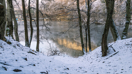 Karst deep-water lake in the mountains. Lake in winter with a view of snow-covered trees. Trees in the snow growing on the mountainside. Clean water in a non-freezing mountain lake. Fog on the lake.