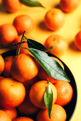 Orange mandarins clementine with green leaves in black plate on a yellow background. Top view