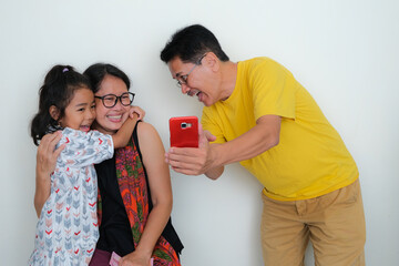 Father, mother and daughter laughing together looking at smartphone