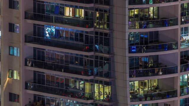 Night view of exterior apartment colorful building timelapse. High rise skyscraper with glowing lights in windows. Lights reflected from glass surface