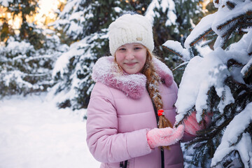 Obraz premium a girl stands near a snowy Christmas tree in winter and throws up snow