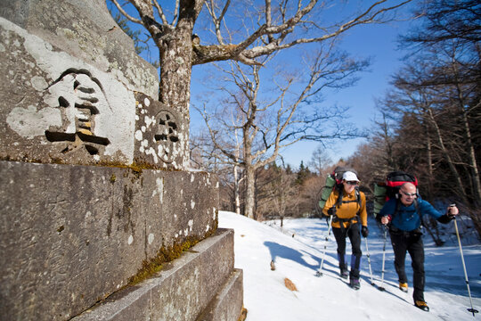 Two people are hiking on a trail next to a wall with Japanese characters on it in Mount Fuji National Park, Honshu, Japan .