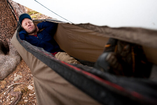 A man takes a short rest in a hammock with a rain fly during rainy weather in the Snowy Range, Wyoming.