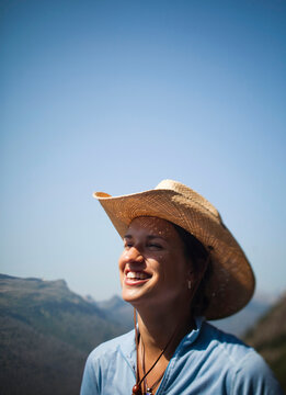 A portrait of a young woman laughing while wearing a cowboy hat with a blue sky in the background.