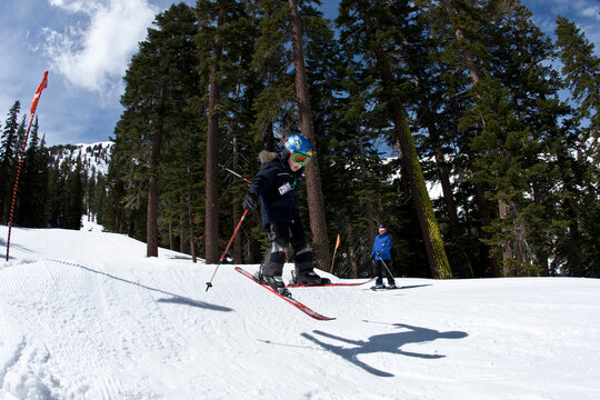 Young skier jumping in a terrain park while his instructor looks on.