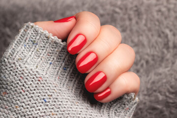 Female hand with beautiful manicure - red nails on gray fluffy knitted fabric. Nail care concept