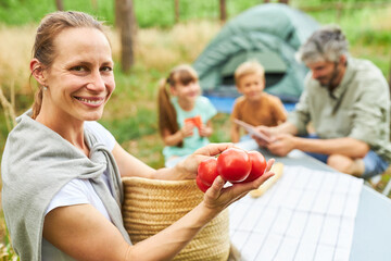 Fototapeta na wymiar Smiling woman holding tomatoes by family in forest