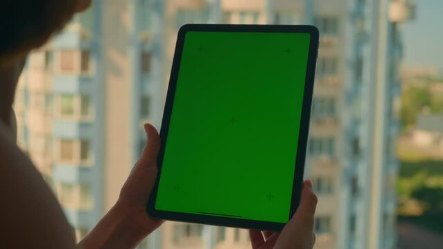 woman standing in front of open window using digital tablet with green screen view on cityscape