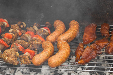 Cooking meat skewers with vegetables, sausages and steakes over the coals on barbecue grill with smoke.
