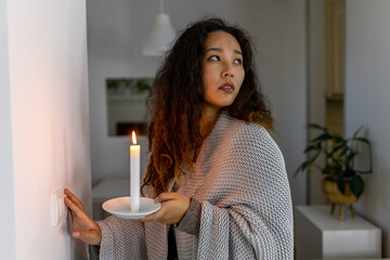 Energy crisis. Hand in complete darkness holding a candle trying to turn on light during a power...