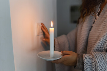 Energy crisis. Hand in complete darkness holding a candle trying to turn on light during a power...