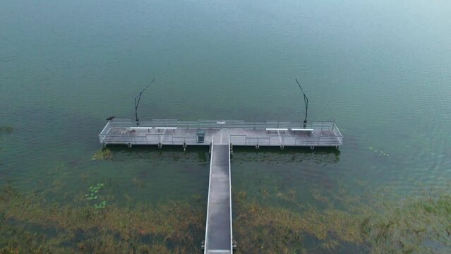 Flyover of fishing dock and aerial reveal of Starke Lake and cloudy sky in Ocoee, Central Florida.  Ocoee is a family oriented town with restaurants, breweries, bars, and shopping.