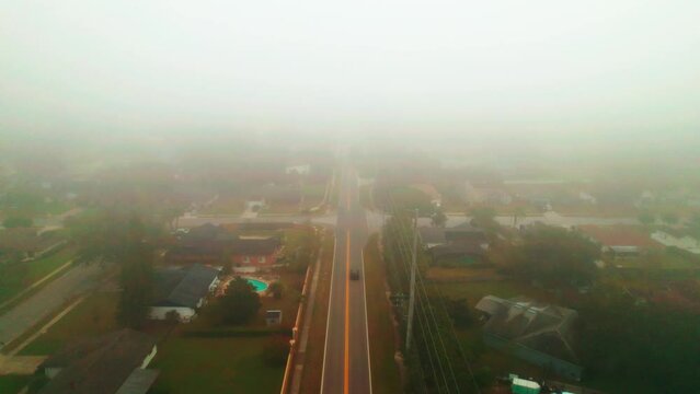 Aerial reverse flyover of foggy and misty road through city of Ocoee, Florida with solo vehicle driving.  Ocoee is a family oriented town with many neighborhoods.