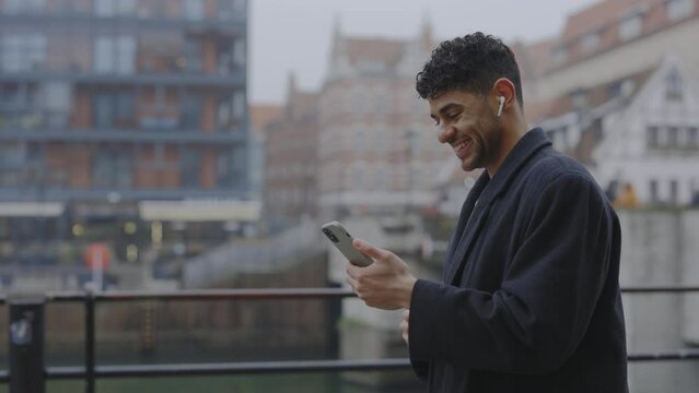 Multi Ethnic Man Is Video Calling His Family Wearing Earphones Walking At City Centre In The Winter Time. Male Boss Wearing Suit Are Speaking On The Video With Clients