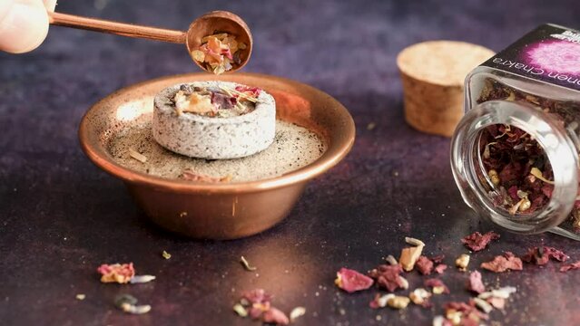 Burning aromatic incense resin (boswellia, frankincense), dried herbs and rose blossom petals. A woman's hand puts the incense with a copper spoon on the glowing incense charcoal