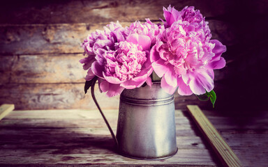 Pink flowers in zinc vase on wooden background There is an old wooden background and black, pink flowers in a zinc vase.