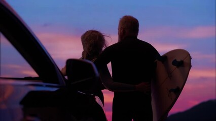 Portrait of mature adult 60s Caucasian surfers couple enjoying the view of beautiful sunset over the ocean