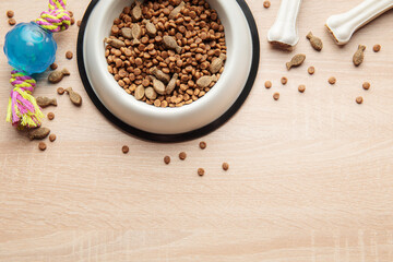A bowl with dog food, dog treats and toys on a wooden floor.