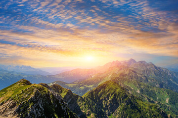 Panorama of a mountain range with alpine meadows during sunset with beautiful sky cloudscape.