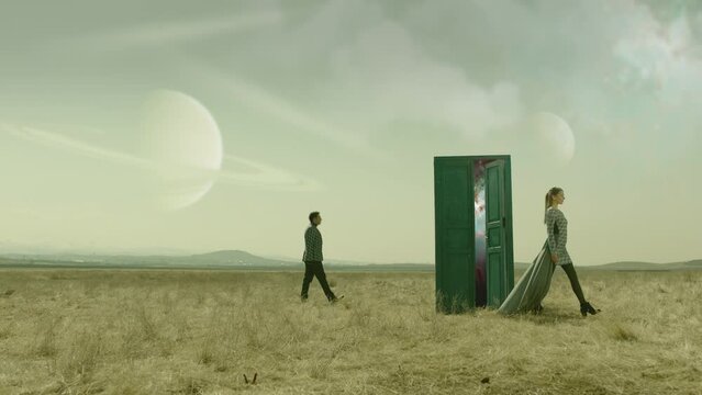 Couple walking on field near door . Young stylish man and woman stand on meadow field . Futuristic Fashion concept . Surrealistic scene . Way to another planet . Planets at day in the sky . Surrealism