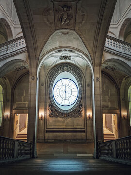 Louvre Palace symmetric architectural details of a hall with stone staircase, ornate railings, different corridors and am ornate clock type window in center, Paris, France