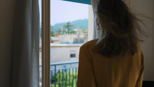 Woman enjoys summer breeze while standing in front of the window.