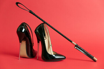 Black shiny high heel shoes and a whip on a red background