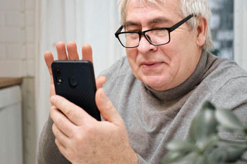 Hoary old man looking at web camera, holding phone, talking with children, wife online. Senior grandpa smiling chatting with friends, family via video call. Modern technologies and older generation.