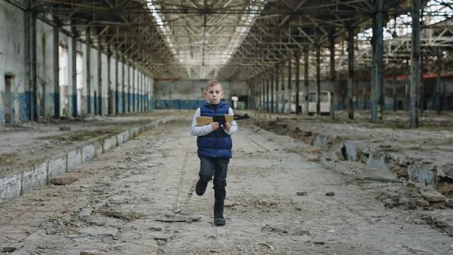 Child is going holding a toy gun against a background of devastation place. Boy games. War. Little boy playing in war