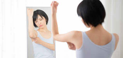 鏡で二の腕をチェックしている若い女性　ダイエットイメージ	