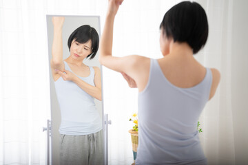 Fototapeta na wymiar 鏡で二の腕をチェックしている若い女性　ダイエットイメージ 