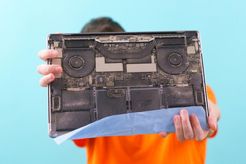 A man holding an opened dirty and dusty laptop on a blue background. Laptop. Repair. Cleaning....