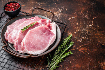 Raw pork chop steaks in steel tray with rosemary. Dark background. Top view. Copy space