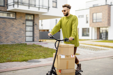 Man drives electric scooter, delivery cardboard boxes on street in residential area. Concept of sustainability, delivering and eco-friendly modern lifestyle