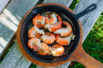 Large fried shrimp lay on a pan with a wooden board, healthy seafood cooked outdoors in a rustic style, prawns fried in oil with aromatic spices