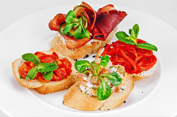 White toasted bread sandwiches with tomato slices, red fish, ham, and white cheese, garnished with green salad leaves; traditional Italian bruschetta for appetizer with vegetables and fish