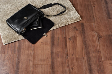 Fashionable men's leather bag open on floor with diary for notes; white rug on brown wood floor
