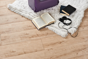 Opened book and black headphones on white mat near the chair against the background of light wooden floor, home environment for quiet time, reading, listening to music or favorite hobby