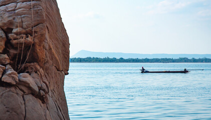 Fototapeta premium Rocks by the lake, blurred background, fishermen on boats. Natural scenery that gives a feeling of strength