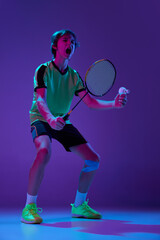 Portrait of teen boy in uniform, badminton player after successful game over blue purple background in neon ligth. Winner