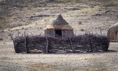 Traditional round clay hut of himba tribe with a fence from dry branches around. Lifestyle of indigenous people of Namibia in Africa. House made of natural materials with tent roof and clay walls. - 558920650