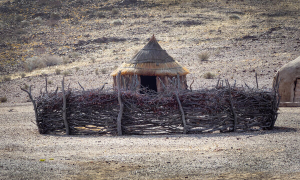 Traditional round clay hut of himba tribe with a fence from dry branches around. Lifestyle of indigenous people of Namibia in Africa. House made of natural materials with tent roof and clay walls.