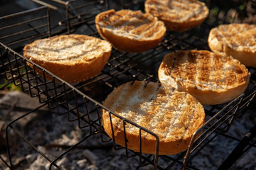 Round buns, lying in rows on the metal grid of the wood-fired grill. The concept of cooking, frying hamburgers. Coal and heat. Selective focus