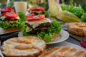 Cooking process, not ready. Big, nice hamburgers with a double patty, fresh vegetables and grilled meat. Sunny day outdoors. Concept of tasty street food. Selective focus