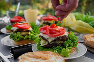 Cooking process, not ready. Big, nice hamburgers with a double patty, fresh vegetables and grilled meat. Sunny day outdoors. Concept of tasty street food. Selective focus