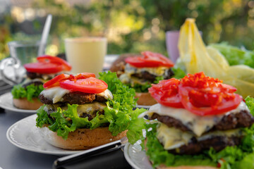 Cooking process, not ready. Big, nice hamburgers with a double patty, fresh vegetables and grilled meat. Sunny day outdoors. Concept of tasty street food. Selective focus